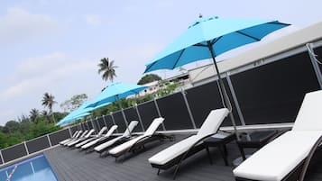 Zona de piscina con sillones de descanso y sombrillas azules.