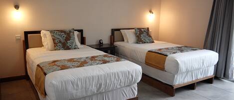 Two single beds with wooden frames and headboards, each with a bedside table and a wall-mounted light.