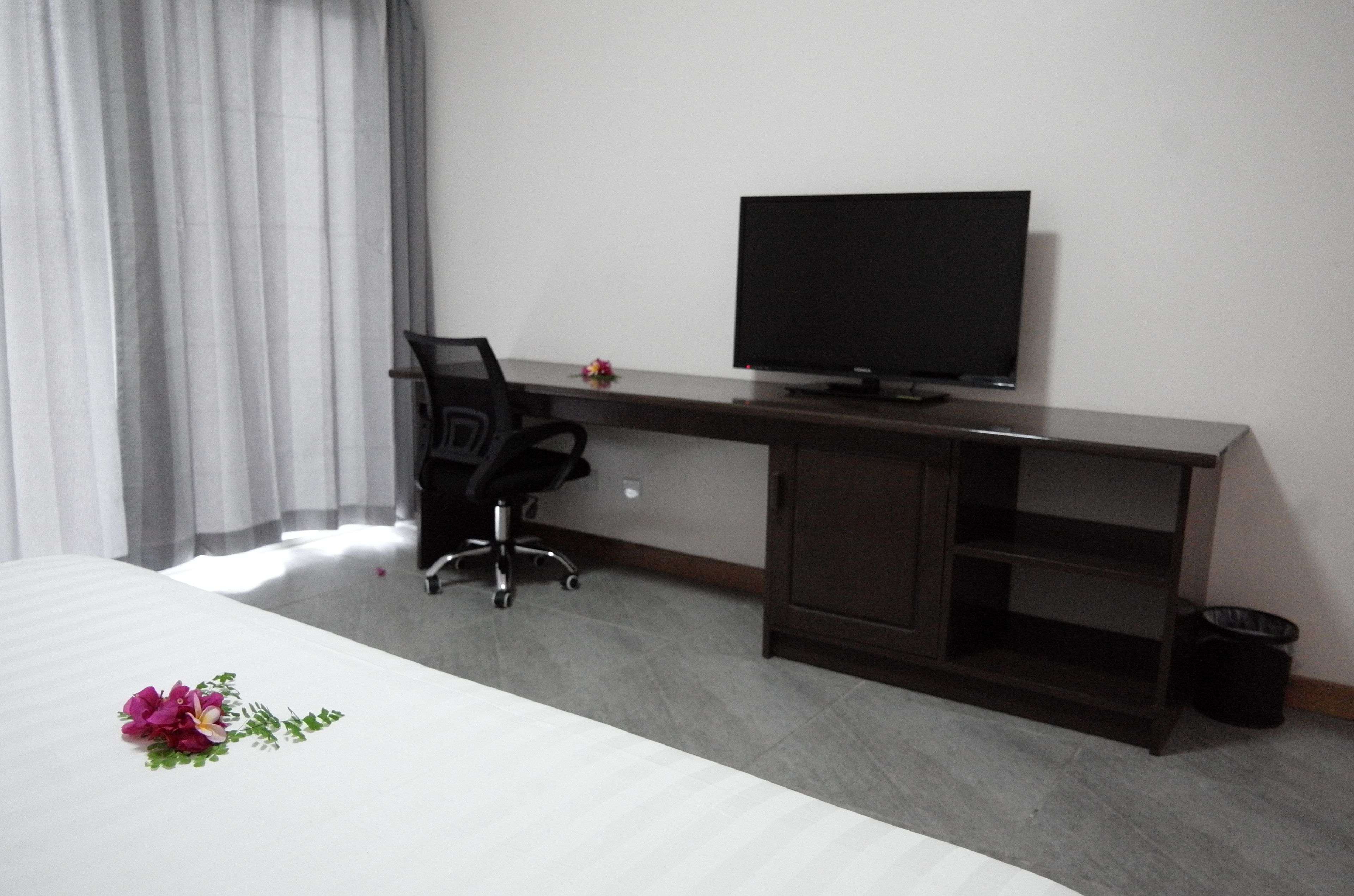 Una habitación de hotel con una cama, un escritorio con una silla, un televisor y un cubo de basura pequeño.