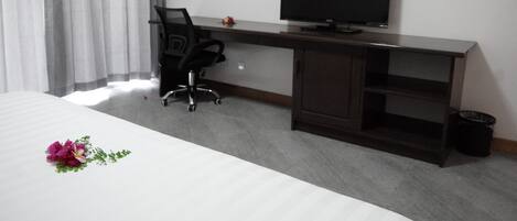 Una habitación de hotel con una cama, un escritorio con una silla, un televisor y un cubo de basura pequeño.