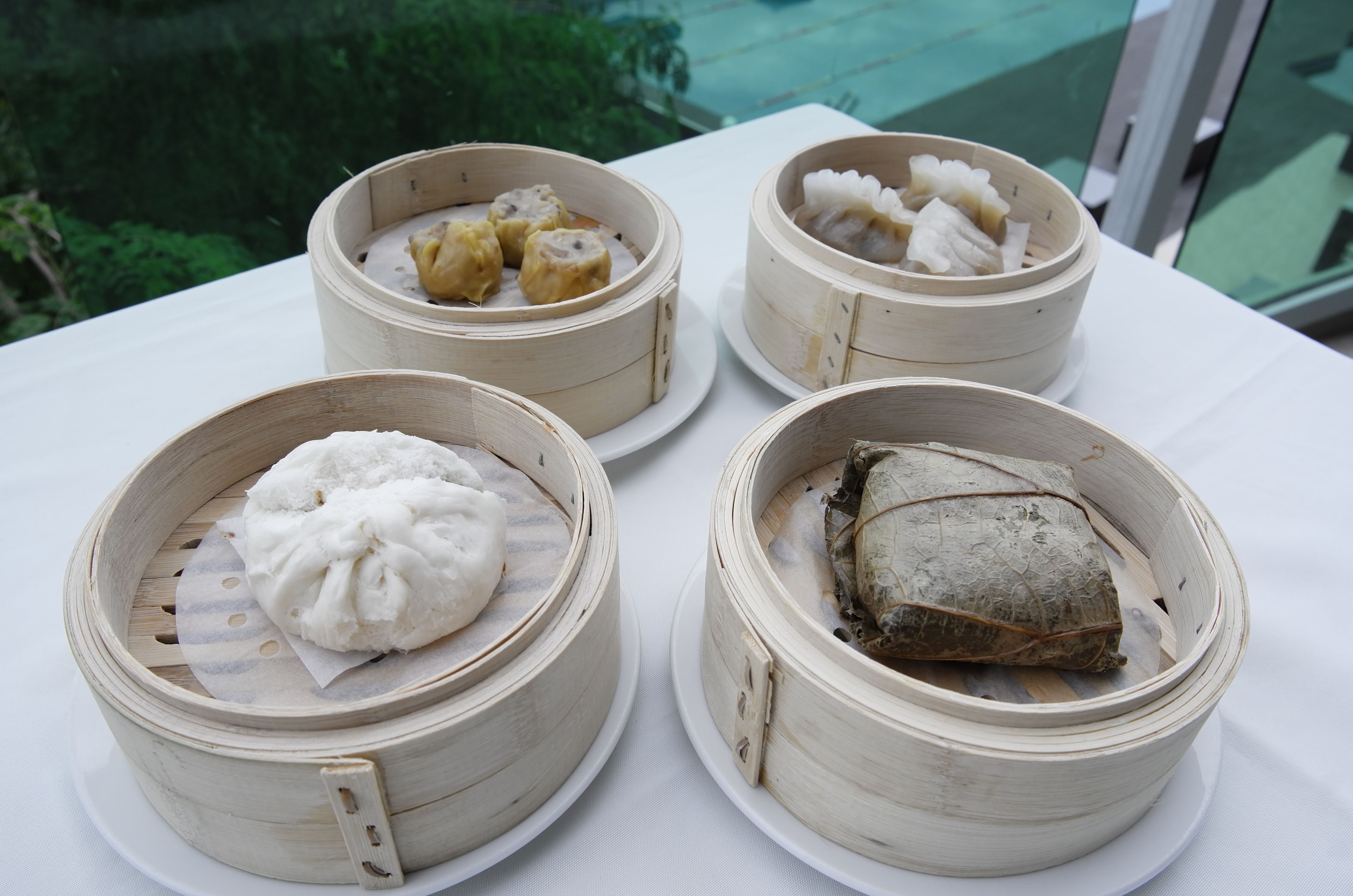 Four bamboo steamer baskets with different types of food on a white table.