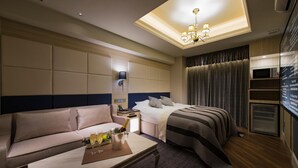 A hotel room with a bed, a sofa, a bedside table with a lamp, a minibar, and a TV. - Hotel Times - Adults Only (Tokyo)