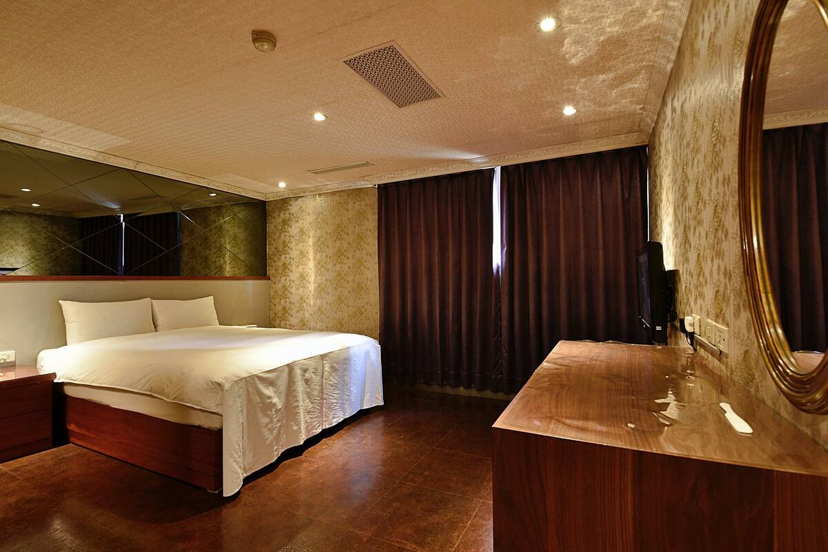 A modern hotel room with a large bed, a wooden vanity, and a large mirror.