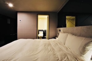 A hotel room with a large bed, a bedside table, a mirror, and a door leading to a bathroom.