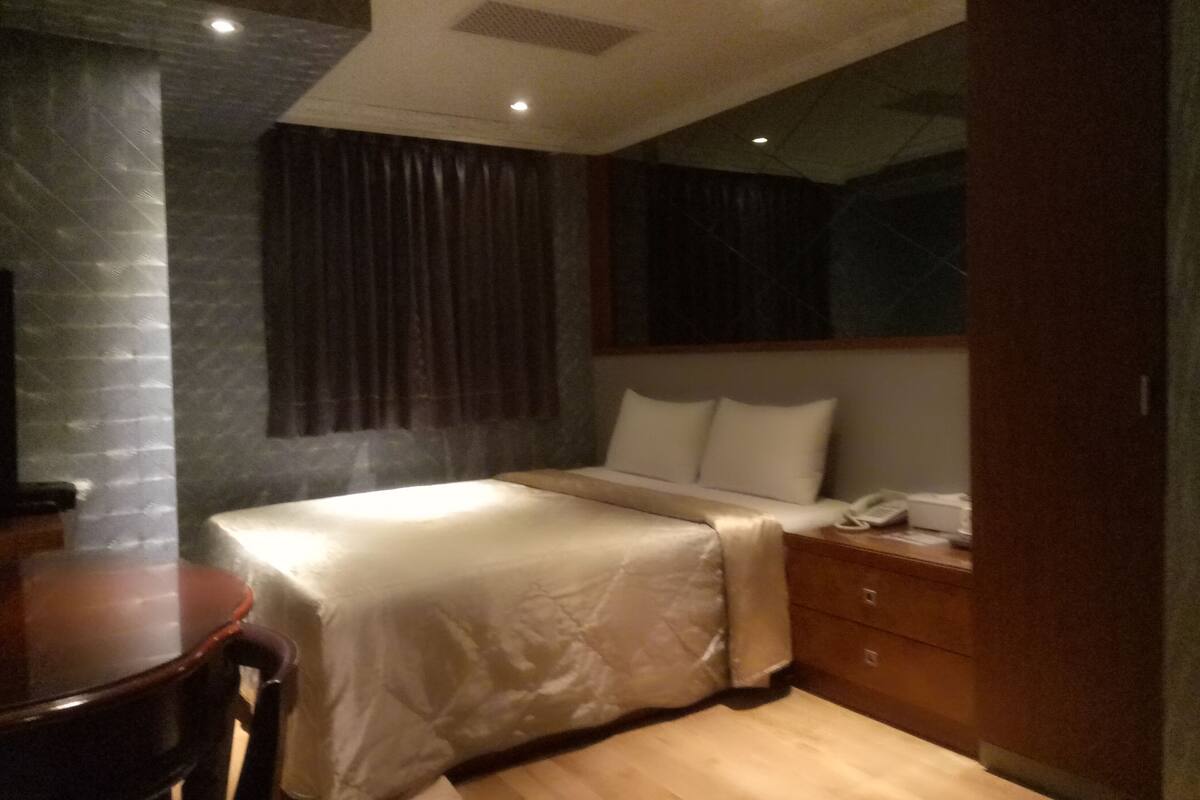 A hotel room with a bed, bedside table, and a desk with a chair.