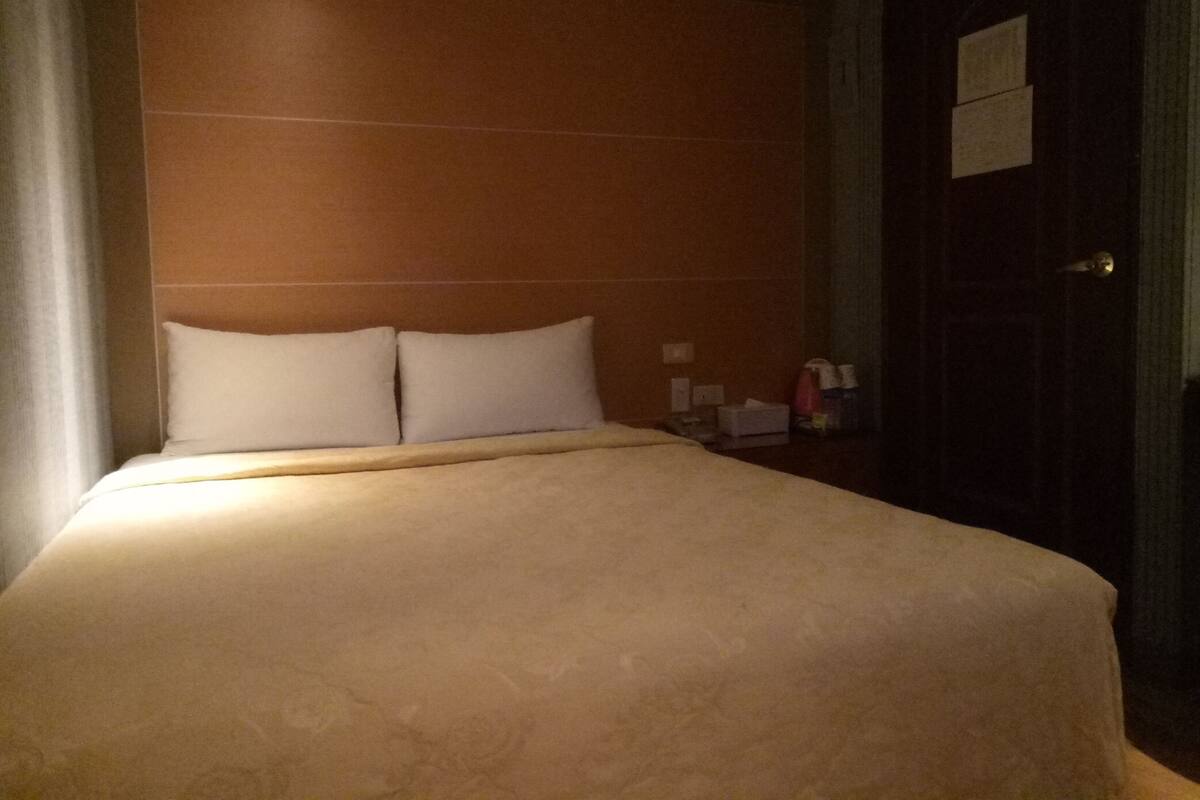 A hotel room with a large bed, a nightstand, and a door.