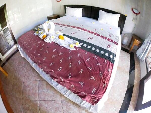 A neatly made bed with a patterned bedspread, a decorative towel arrangement, and a clean, tiled floor.