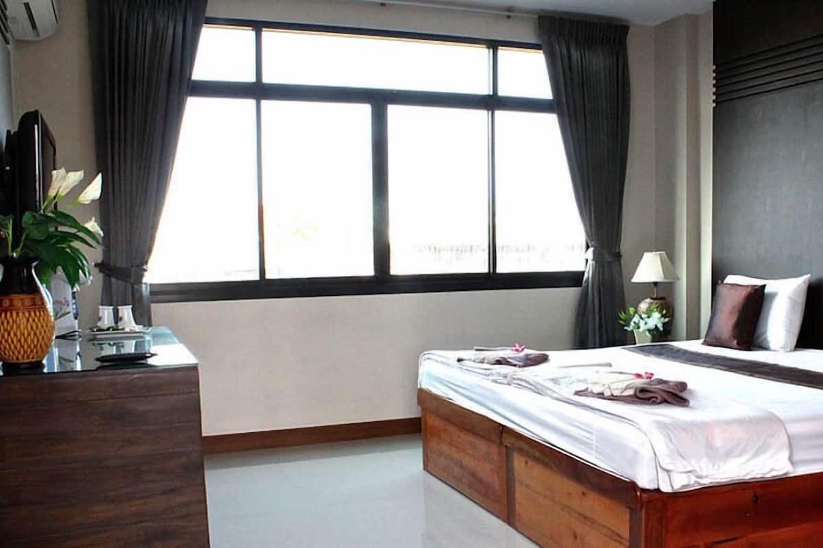 A hotel room with a large bed, a desk with a lamp, and a window with curtains.