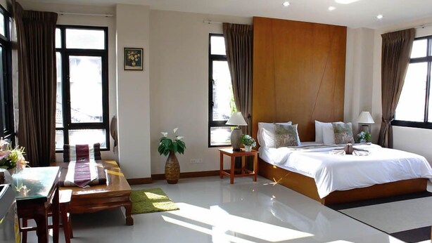 Una habitación de hotel moderna con una cama grande, un escritorio de madera, una mesita pequeña y una planta en maceta.