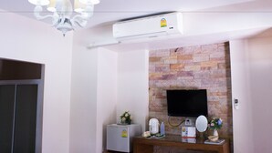 Habitación de hotel con pared de piedra, televisor montado, refrigerador pequeño, cafetera, espejo y lámpara en el techo.