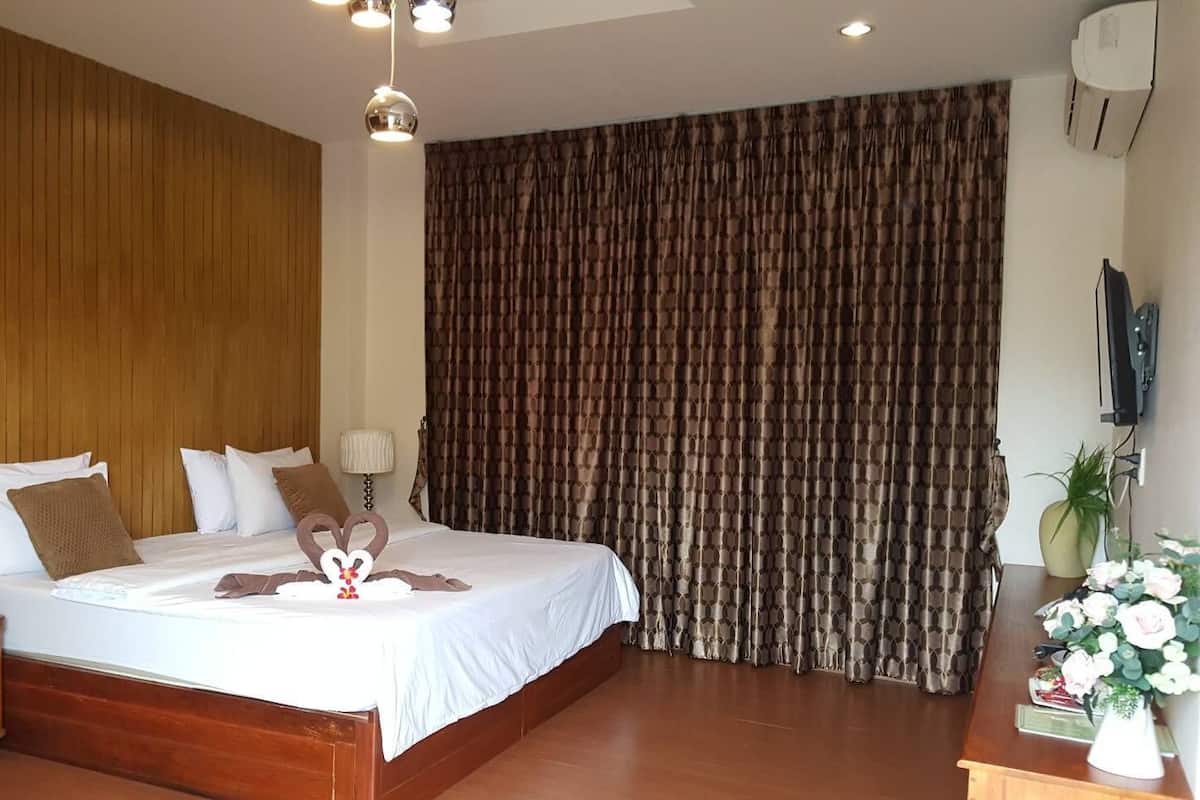 A hotel room with a large bed, wooden paneling on one wall, a curtain, a desk with a lamp, and a potted plant.