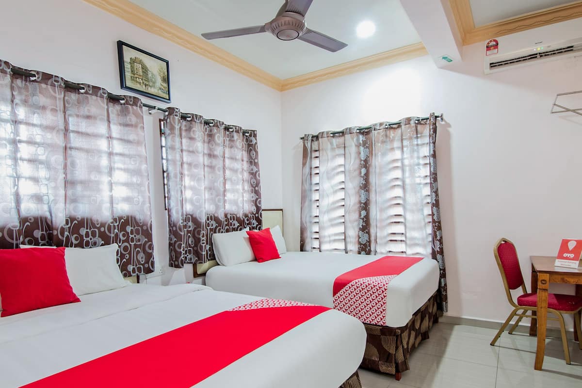 A hotel room with two beds, a ceiling fan, an air conditioning unit, and a small table with a chair.
