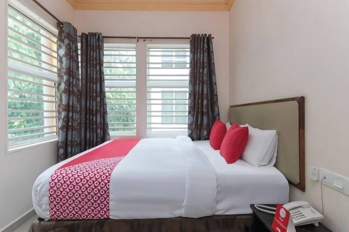A hotel room with a bed, curtains, a window, and a bedside telephone.