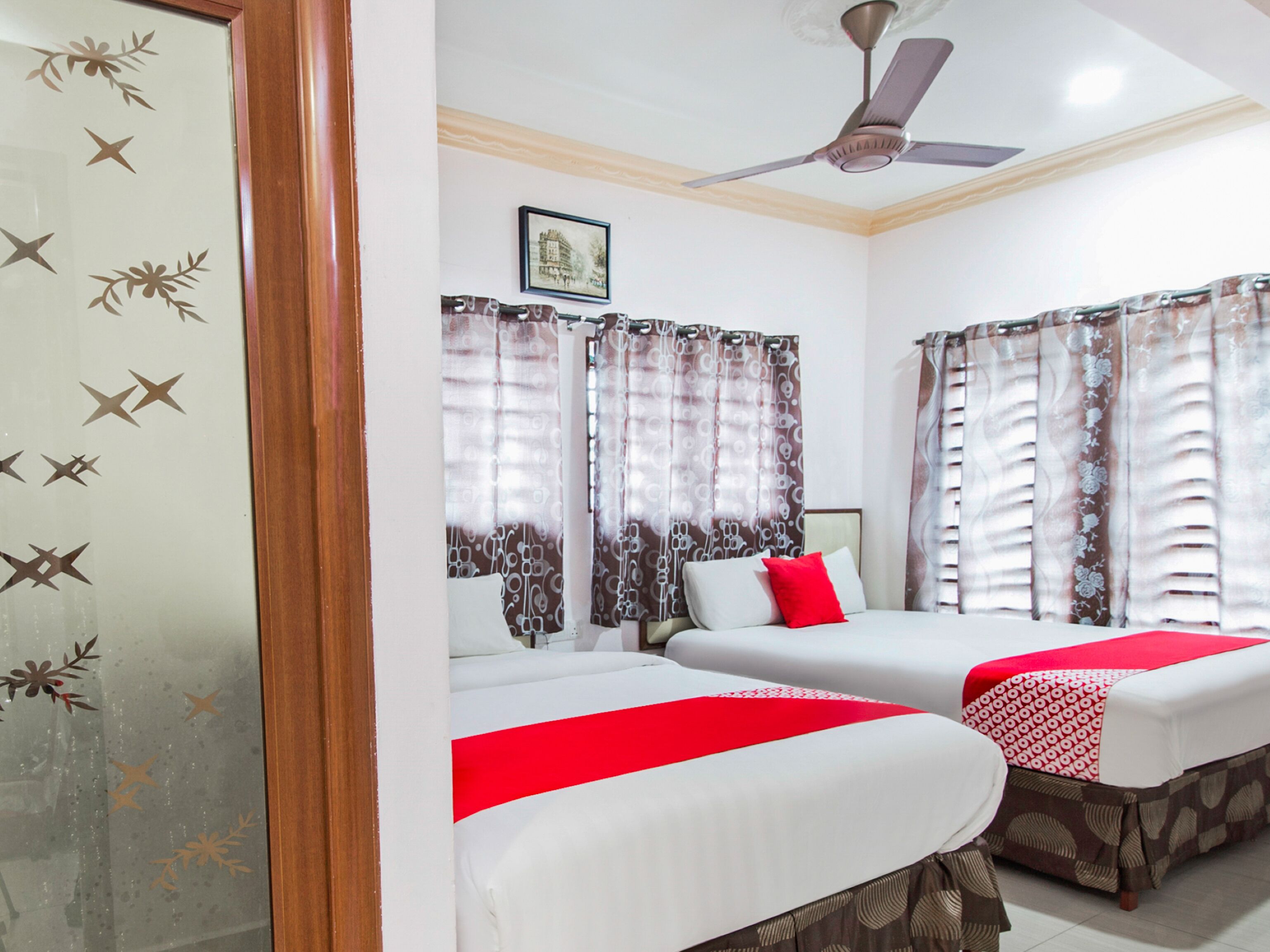A hotel room with two beds, a ceiling fan, and curtains with a floral pattern.