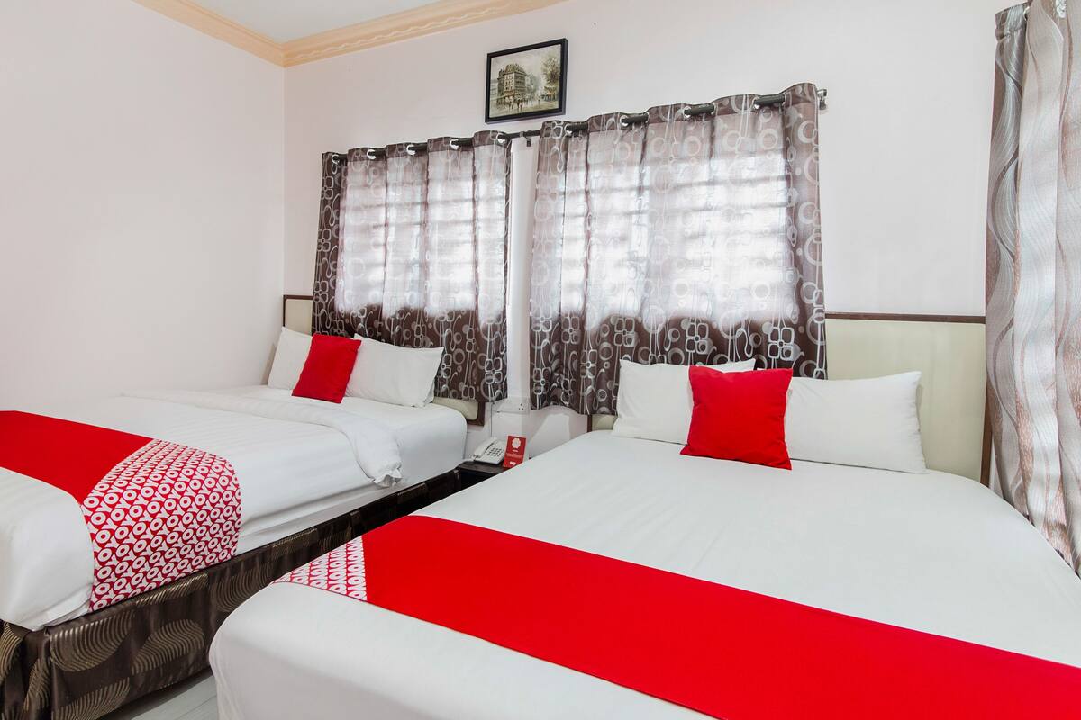 A hotel room with two beds, each with white bedding and red accents, and a small table between them.