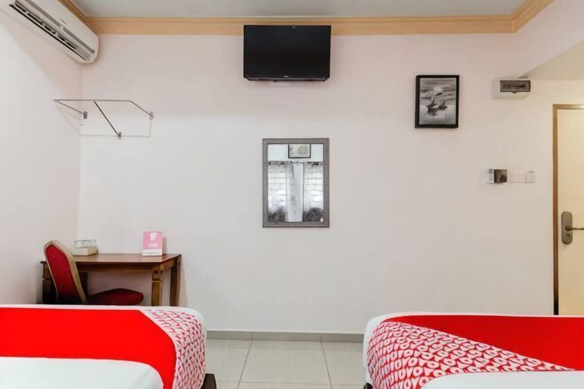 A hotel room with two beds, a desk with a chair, a television, a window, and a door.