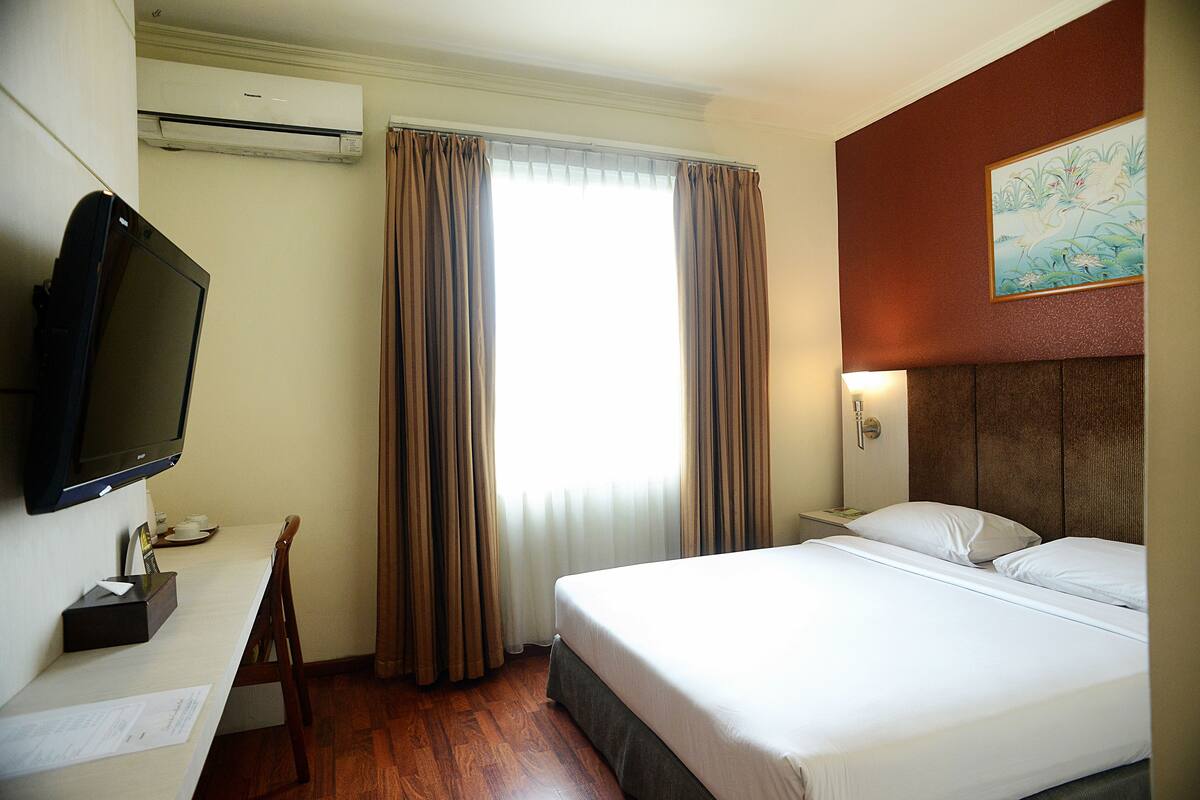 A hotel room with a bed, a desk with a computer, a television, and a window with curtains.