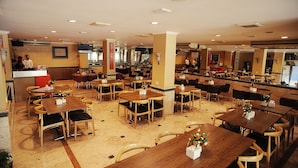 A spacious restaurant with multiple dining tables and chairs, a central bar area, and a television mounted on the wall. - Hotel Anugerah Palembang (Palembang)