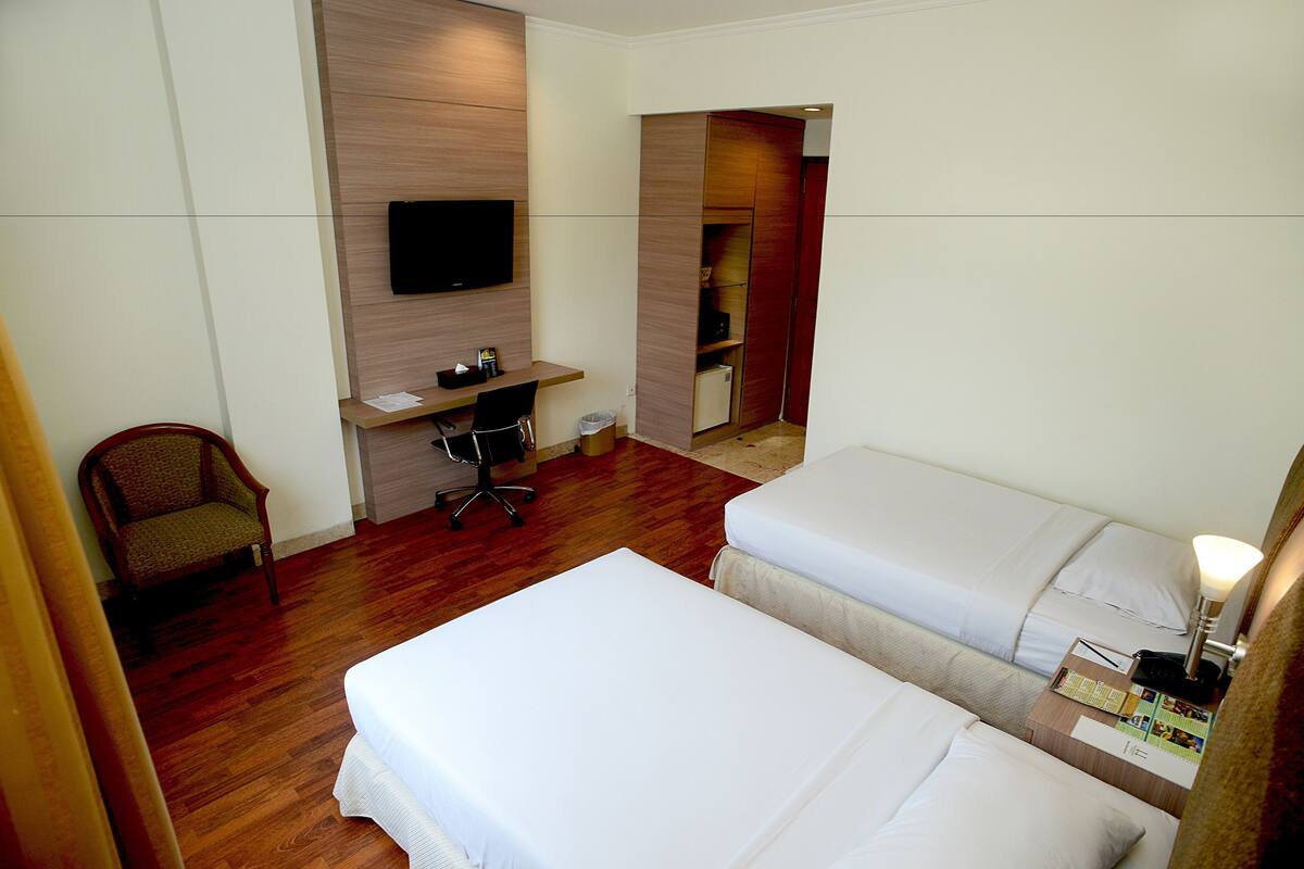 A hotel room with two beds, a desk, a chair, a TV, and a wardrobe.