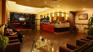 A hotel lobby with a reception desk, seating area, and a glass coffee table with flowers. - Hotel Anugerah Palembang (Palembang)