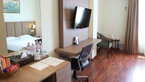 A hotel room with a bed, desk, chair, television, and a small table with a trash bin. - Hotel Anugerah Palembang (Palembang)