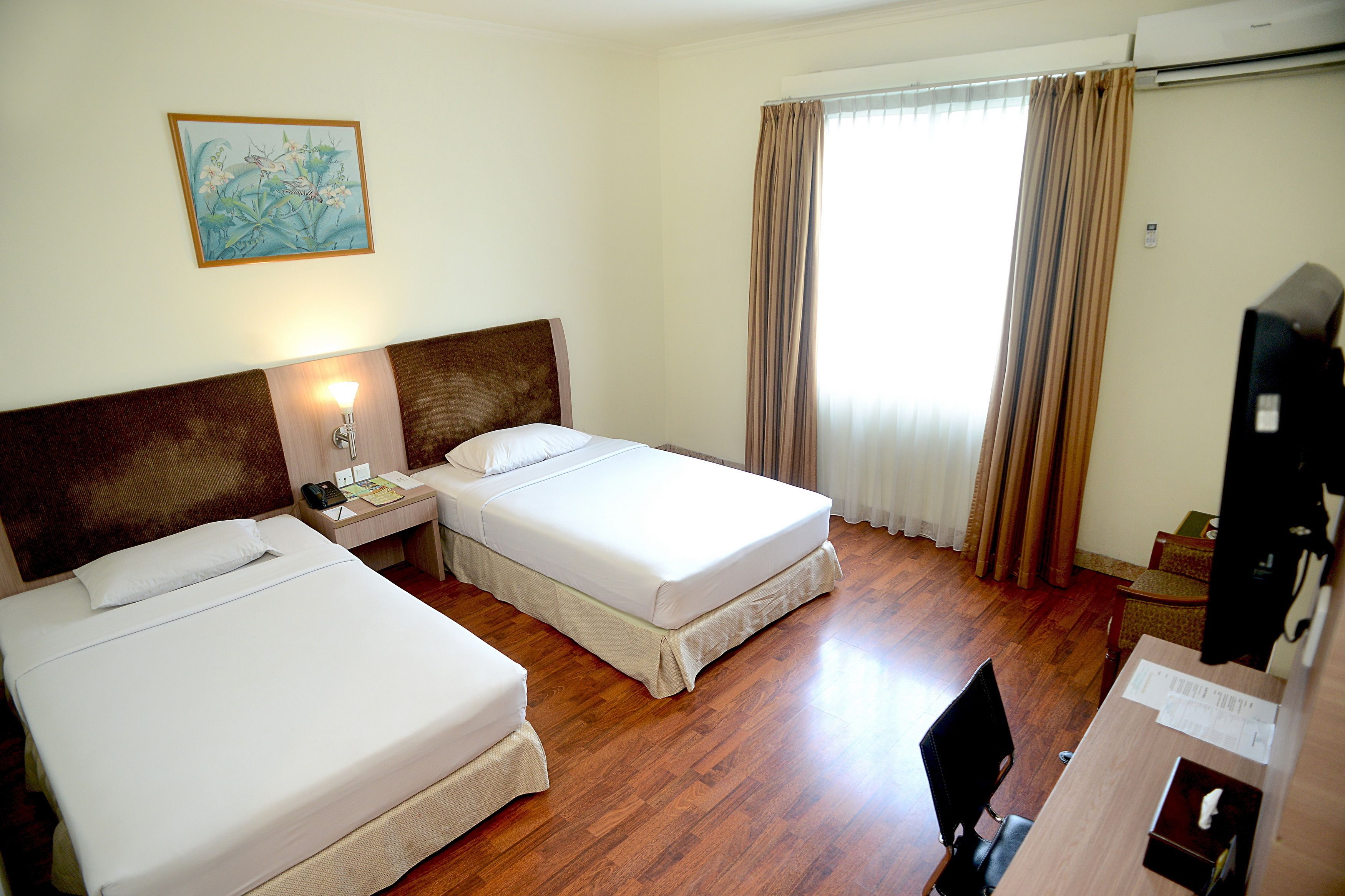 A hotel room with two beds, a desk, a chair, and a television.
