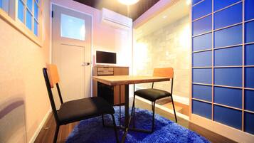 A room with a blue carpet, a wooden table, two chairs, a TV, and a wall with a grid pattern.