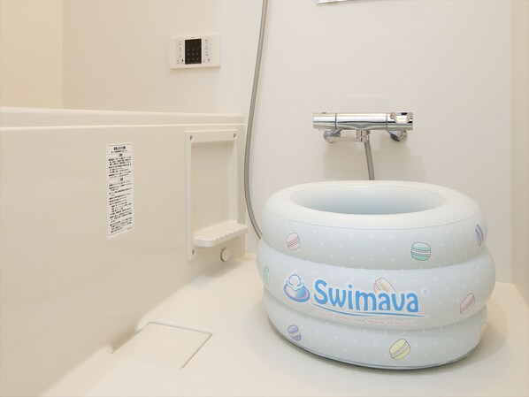 A bathroom with a white sink, a white toilet, and a white shower area. There is a white wall with a small electrical outlet and a white shelf.