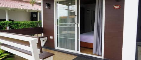 Una habitación con cama, un banco y un ventanal corredera que da a un balcón.