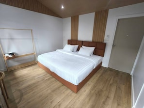 A modern bedroom with a large bed, a wooden floor, a wall-mounted shelf, and a door.