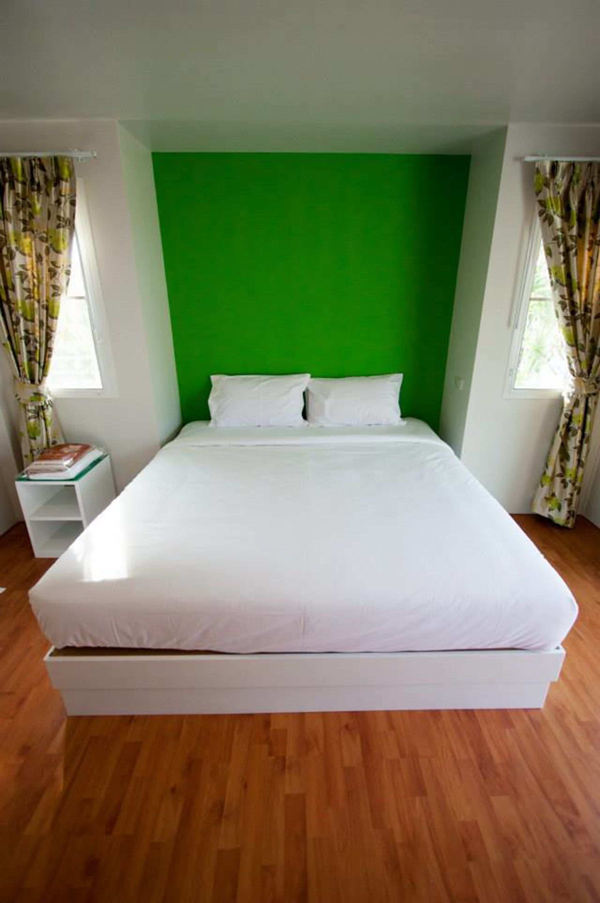 A single-bed room with a green accent wall, white bedding, and wooden flooring.