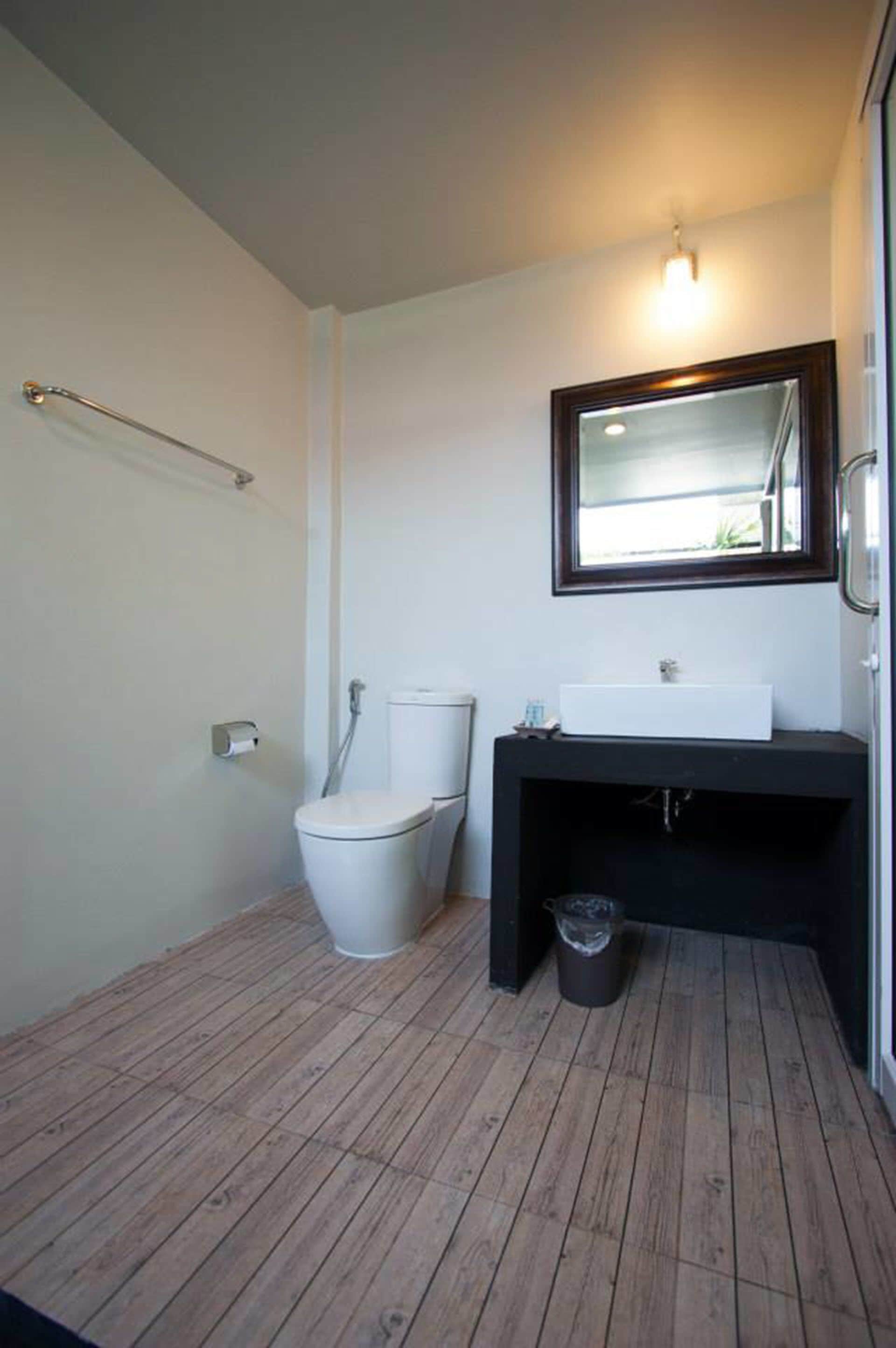 A modern bathroom with a white toilet, a black sink, and a mirror above it.