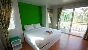 Un dormitorio moderno con una pared de acento verde, una cama grande, una mesita de noche pequeña y un balcón con vistas a la vegetación.