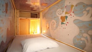 A room with a bed, a window with curtains, and a wall with a colorful abstract design. - BaseInn Komagome Tokyo - Hostel (Tokyo)