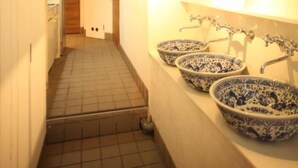 A narrow hallway with a tiled floor leading to a bathroom with three blue and white patterned sinks and a mirror above them. - BaseInn Komagome Tokyo - Hostel (Tokyo)
