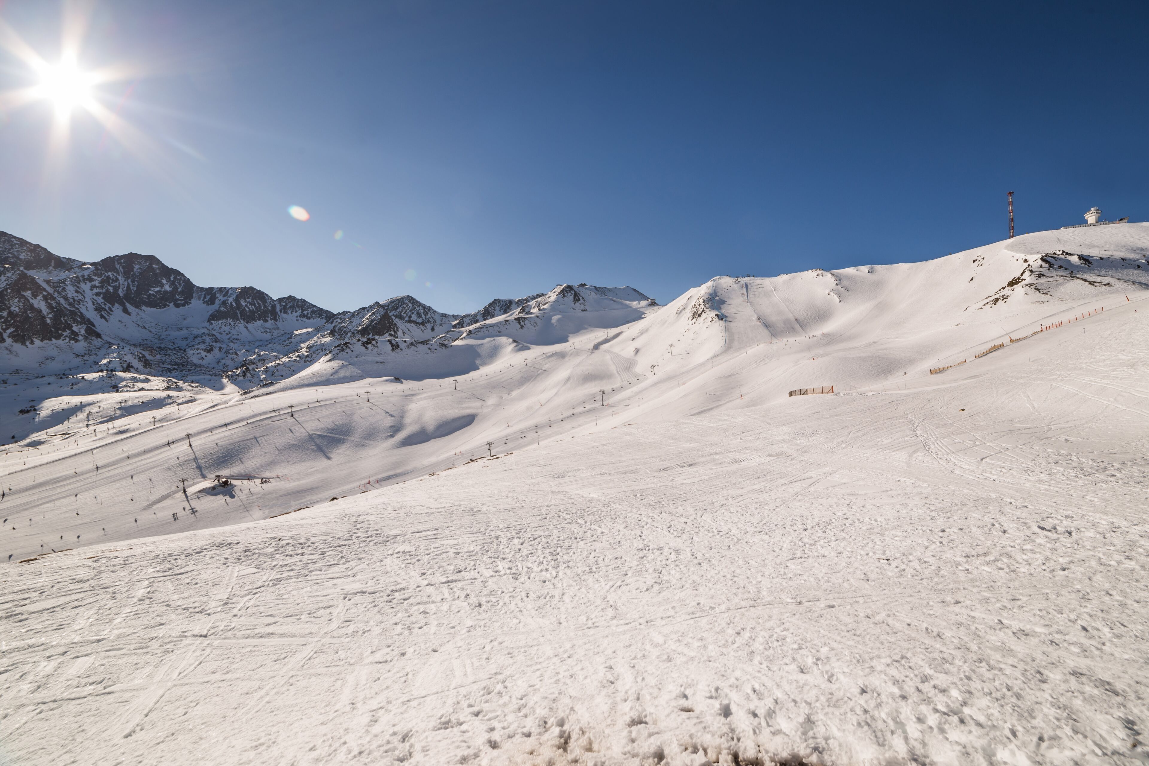 Pista de esquí nevada con cielo despejado y montañas al fondo.