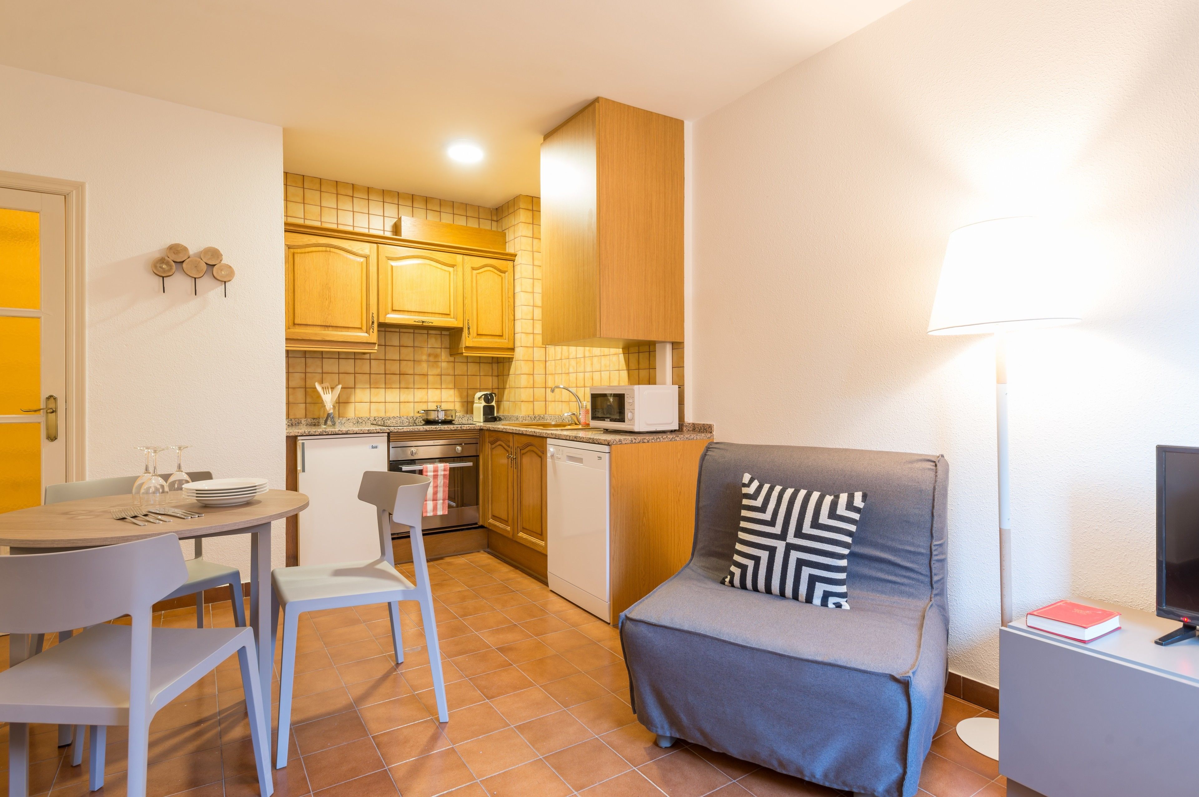 A compact kitchen with wooden cabinets, a microwave, and a dining area with a table and chairs.