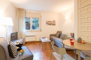 A cozy living room with a sofa, a coffee table, a TV, and a window with curtains. - Pierre & Vacances Andorra Alba (El Tarter)