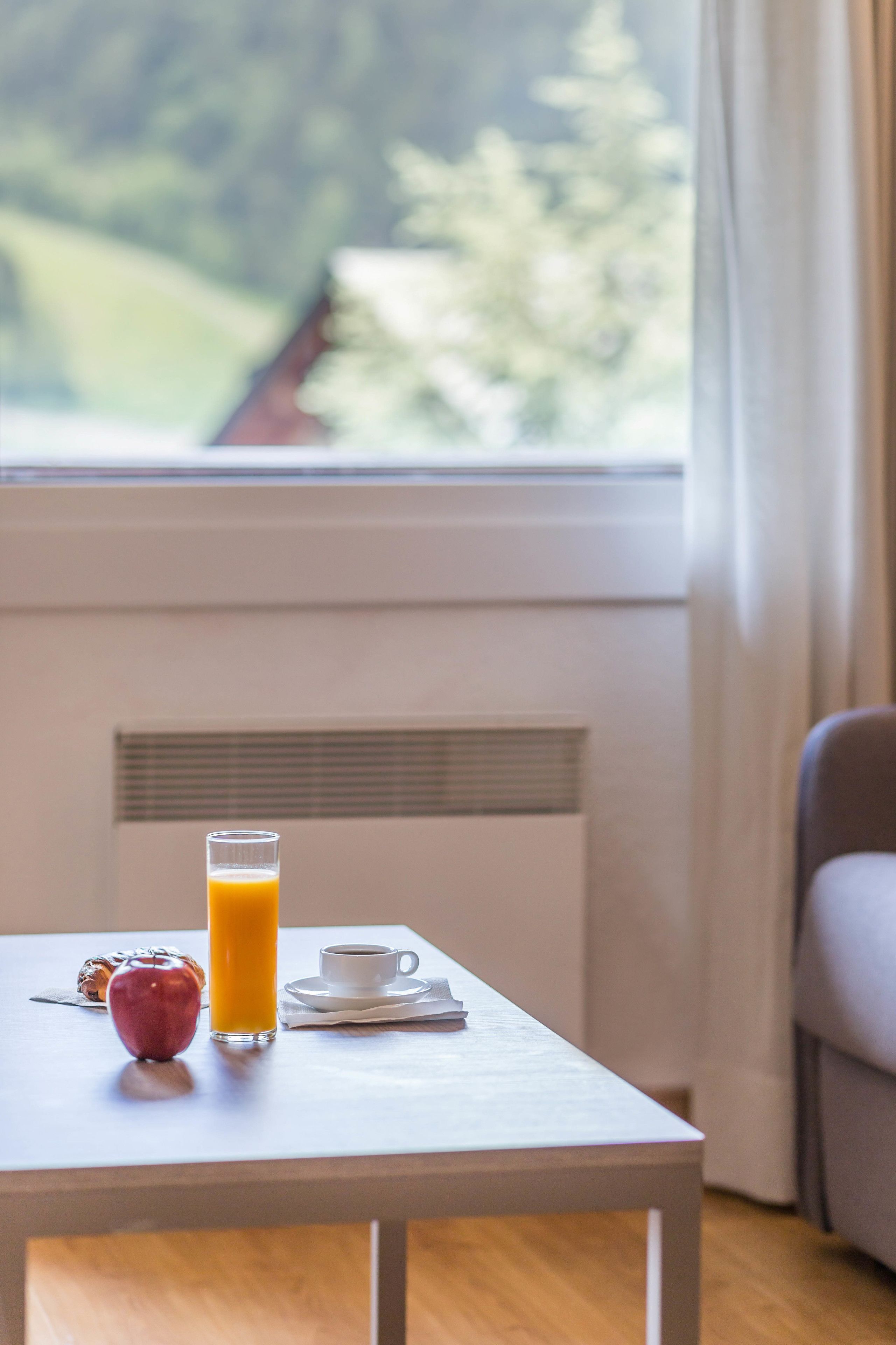 Una mesa de desayuno con un vaso de jugo de naranja, una taza de café y una manzana roja.