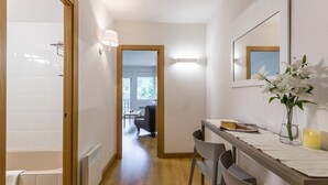 A hallway with a wooden floor, a white bathtub, a table with chairs, a vase with flowers, and a lit candle. - Pierre & Vacances Andorra Alba (El Tarter)