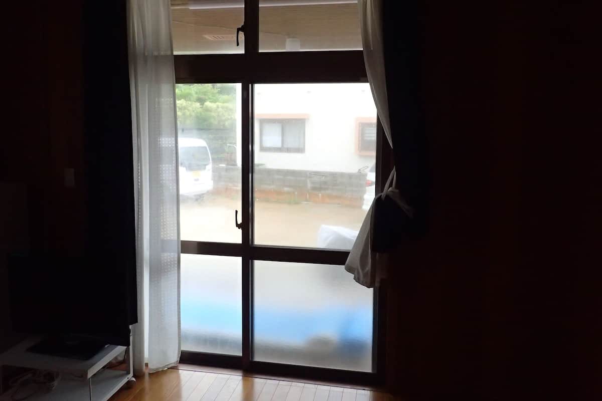 A room with a large window, a white curtain, and a white van outside.