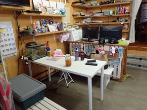 A small, cluttered office with a desk, computer, shelves with various items, and a calendar on the wall. - Sea Blue (Onna)