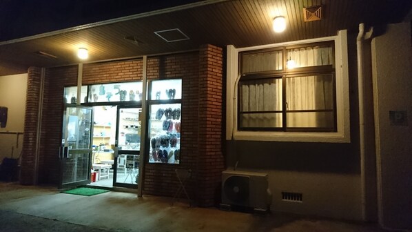 A storefront with a glass door and window, a brick wall, and a small air conditioning unit outside. - Sea Blue (Onna)