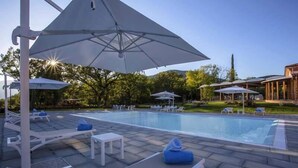 A swimming pool with lounge chairs and umbrellas, surrounded by a landscaped garden and a building with columns. - Tenuta Esdra (Pontecorvo)