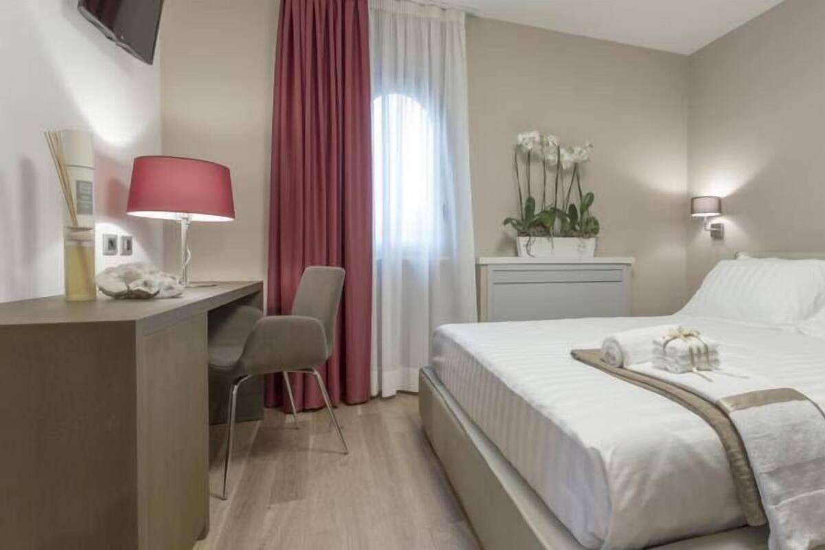 Hotellihuone, jossa on sänky, työpöytä, tuoli, lamppu ja ikkuna, jossa on verhot.