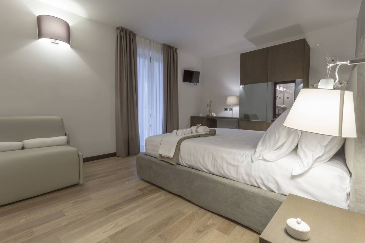 Moderni hotellihuone, jossa on sänky, sohva, työpöytä, lamppu ja televisio.