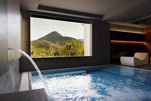 Una piscina moderna interna con vista diretta su un paesaggio montano attraverso un'ampia finestra.