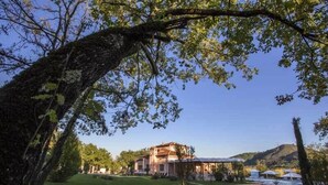 A large, two-story building with a garden in front, surrounded by trees and hills. - Tenuta Esdra (Pontecorvo)