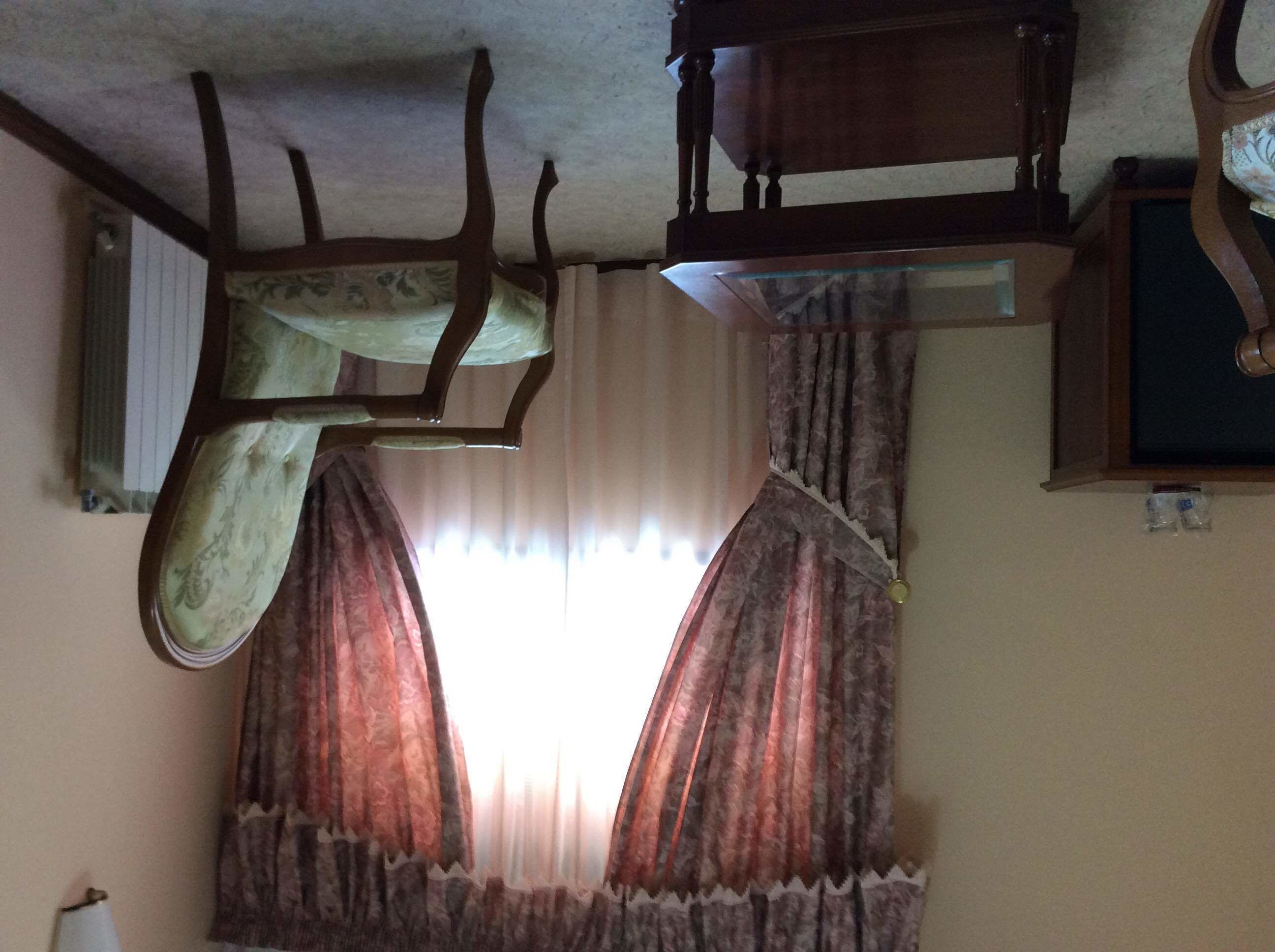 Une pièce avec un plafond en bois, une fenêtre avec des rideaux et une chaise.