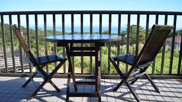 Un balcon avec une table et deux chaises, offrant une vue panoramique sur l’océan et la végétation environnante.